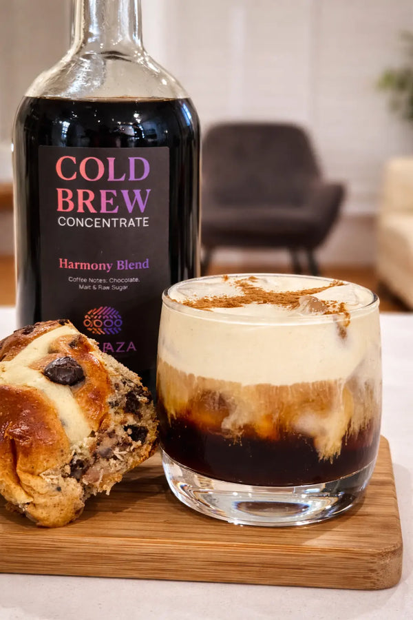 Cold brew concentrate bottle with a layered coffee drink and pastry on a wooden board.